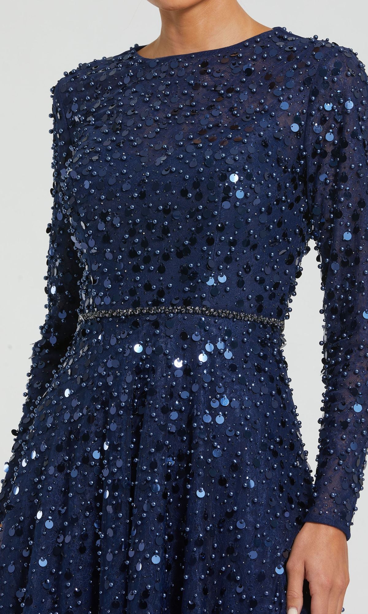 A woman is shown from shoulders to hips wearing the Mac Duggal 11782 Long Sleeve Sequin Formal Gown, a navy blue dress with sequins and a thin beaded waistband.
